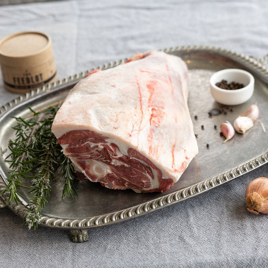 Raw lamb roast cut on a silver tray with herbs and spices on a gray surface